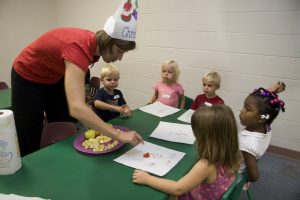 Woman in silly hat helping children with worksheet