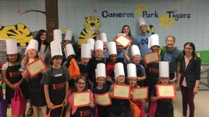 Group of kids wearing chef hats and aprons holding certificates