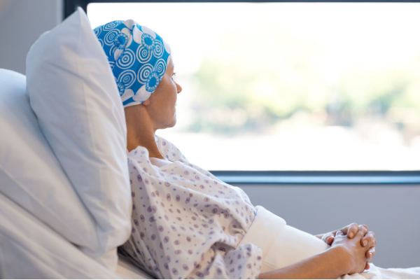 Woman in a hospital bed, wearing a head covering, looking out the window