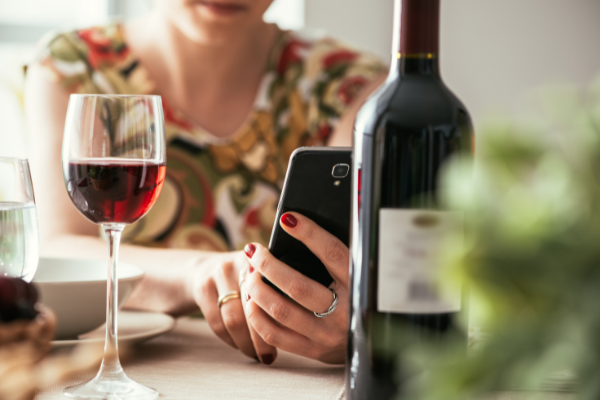 Woman with glass of wine shops for alcohol on phone