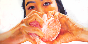 A self-portrait of the artist looking at the viewer, with their hands in front of their face, pulling apart sections of a citrus fruit. Their hands and the fruit are in front of the lower half of their face but you can see their eyes, eyebrows, and hair above the fruit.